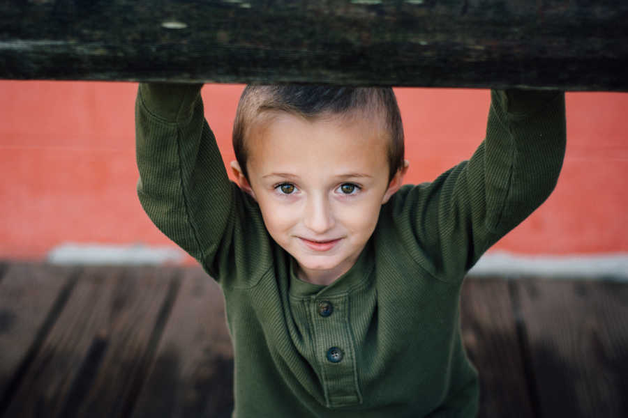 Little boy smiles with arms holding onto beams above him 