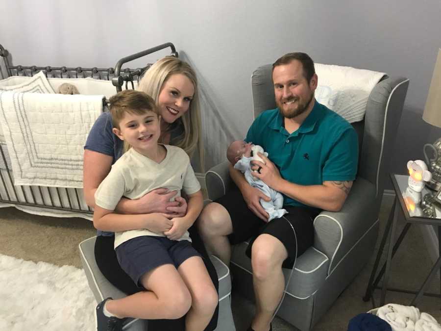 Husband sits in chair with newborn son who finally left NICU beside wife and older son