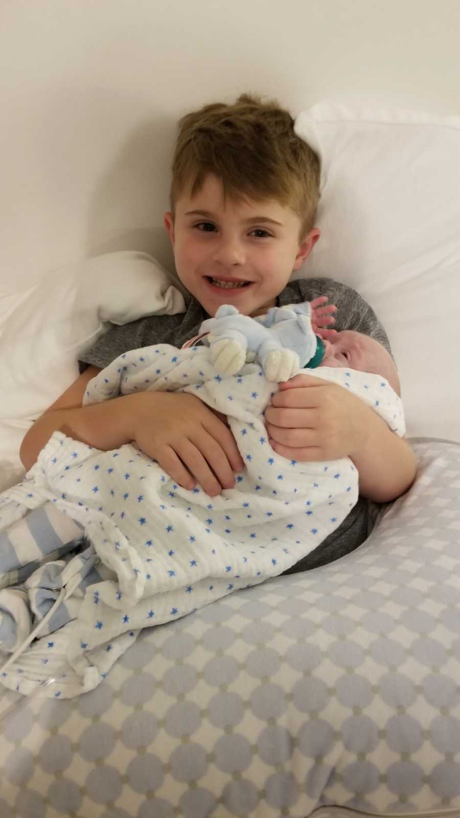 Young boy smiles holding newborn sibling in his lap