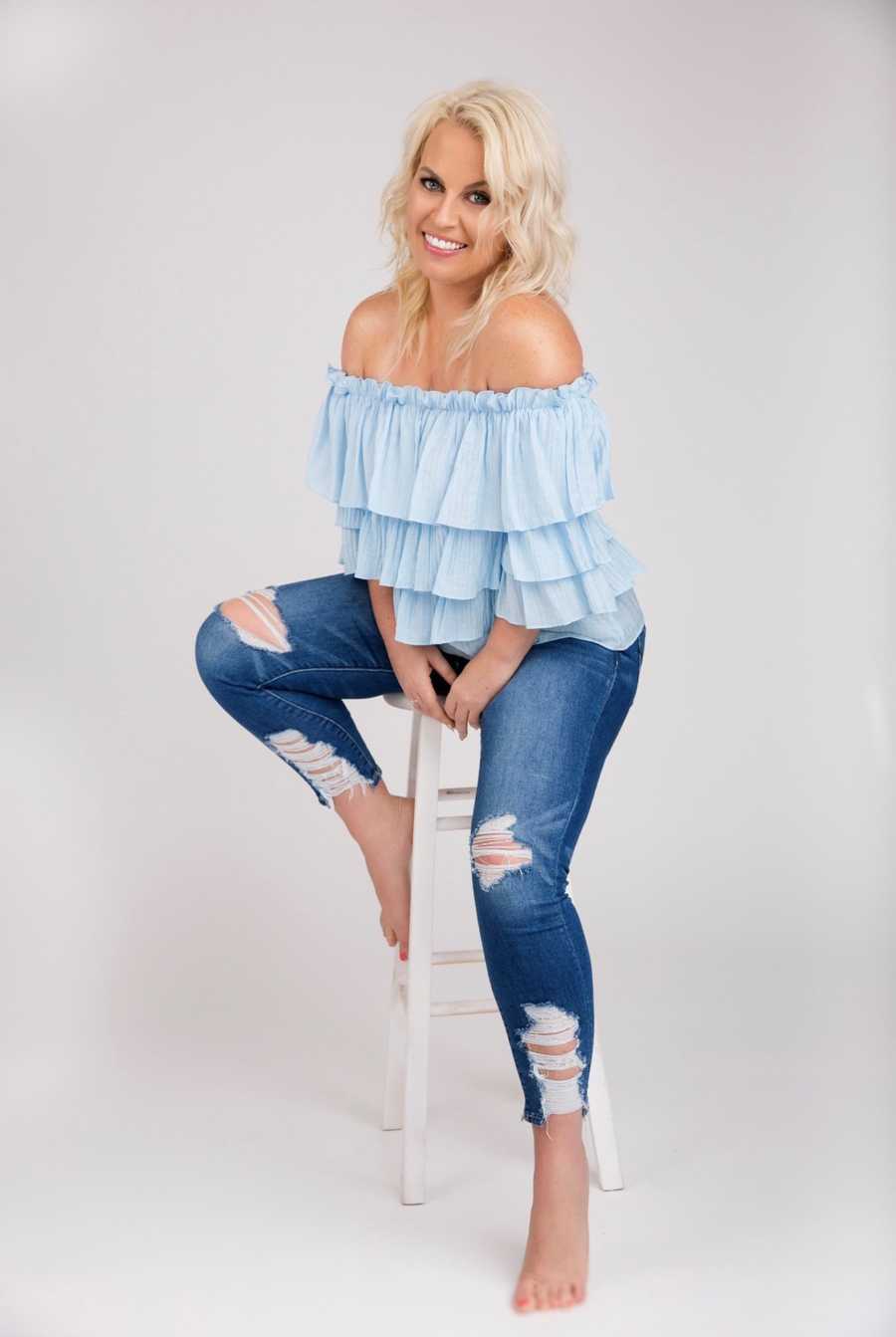 Recovered junkie sitting on white stool smiling in photoshoot