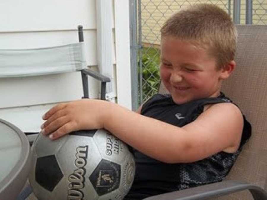 Little boy sits laughing in chair with soccer ball on his lap