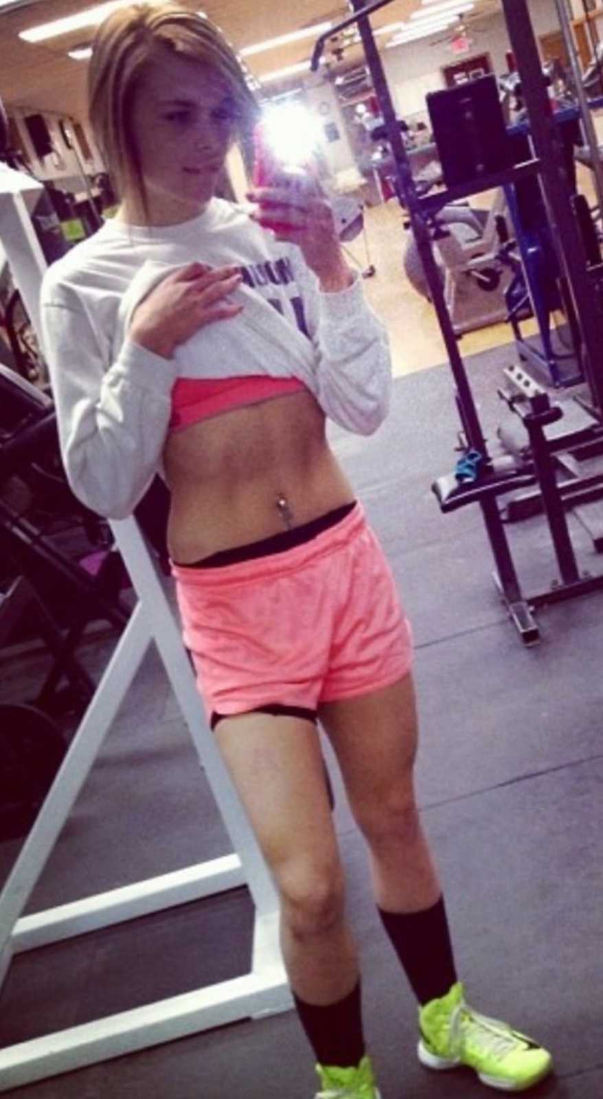 Woman takes a mirror selfie at the gym, showing off her abs