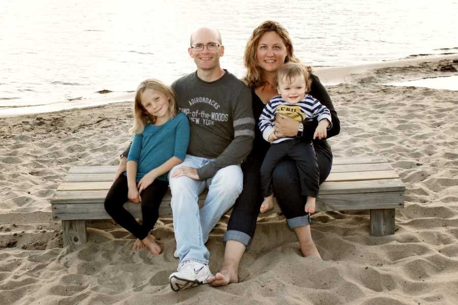 Husband and wife who lost their first born sit on wooden plank on beach with two daughters