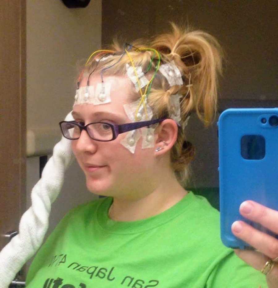 Woman with epilepsy smiles in mirror selfie with wires attached to her head