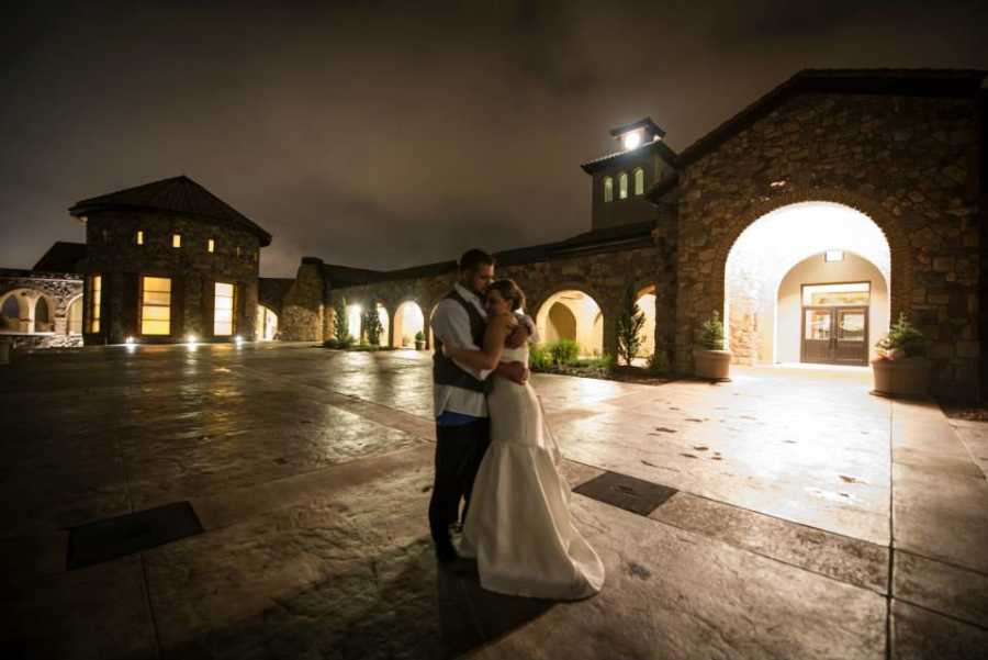 Bride who will have struggles getting pregnant in future, stands hugging groom outside in parking lot at night