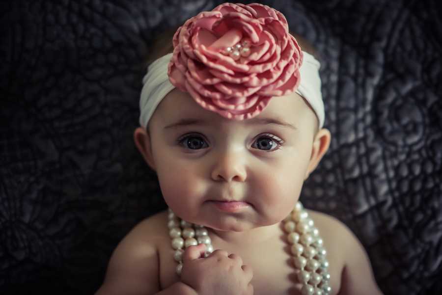 Infant whose mother struggled to get pregnant sitting with pearls and pink flower headband on