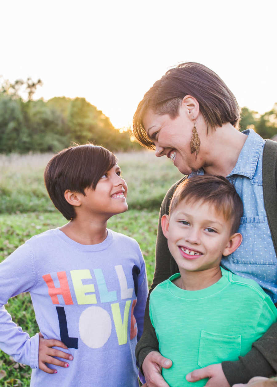 Woman stands with arms around foster child while looking down at other foster child