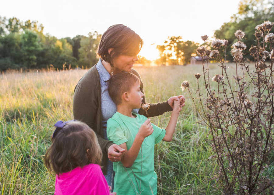 Woman stands in field with foster children picking dandelions