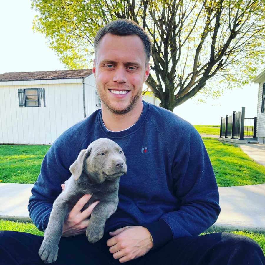 Man who got clean sits smiling in grass with puppy in his lap