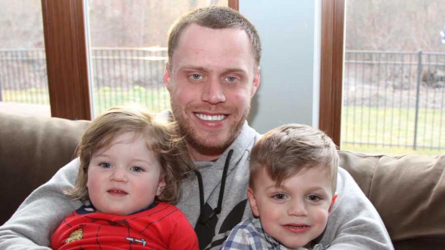 Man who got clean sits on couch with two young children sitting on his lap