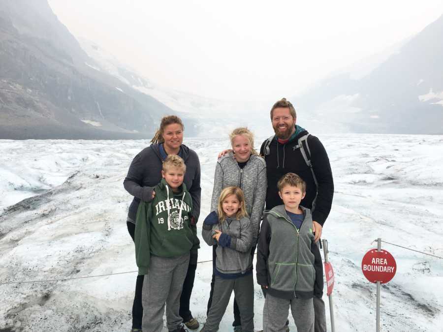 Family of six who travels the US in airstream stand smiling with snowy landscape in background