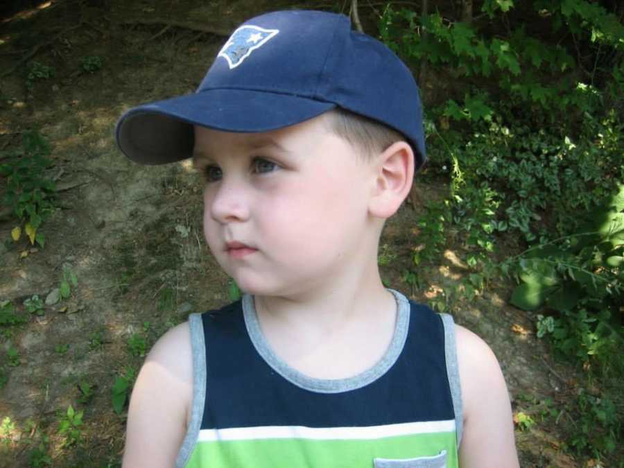 Toddler whose mother doesn't want him to grow up stands looking to side in baseball hat