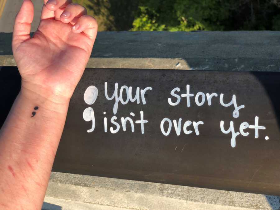 Tattoo of semi'colon on 22 year olds wrist near ledge that has "; your story isn't over yet" written on it