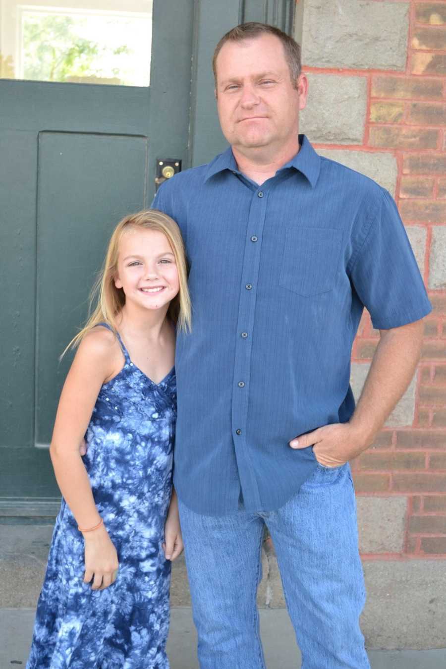 Young girl stands with her dad for a photo while they both wear blue