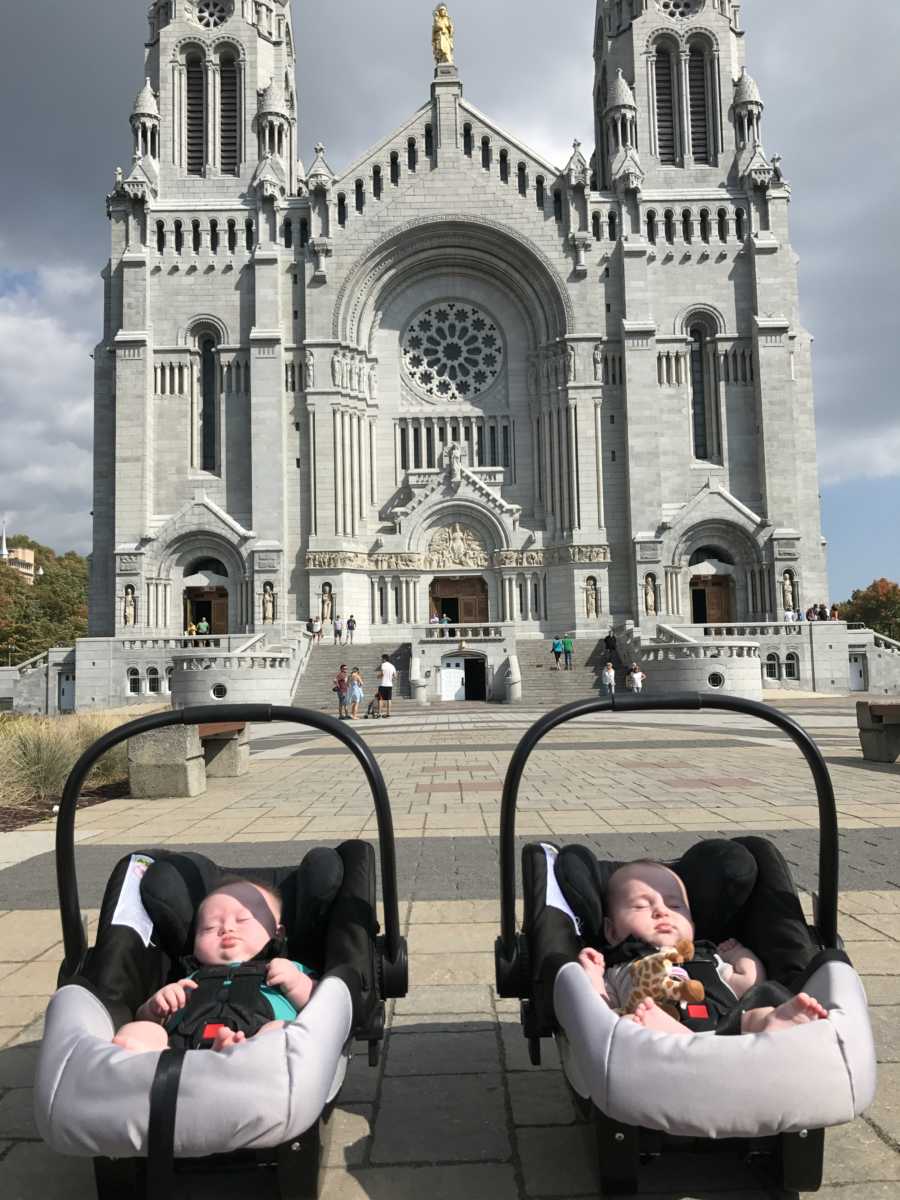 Twins sleeping in car seats on ground in front of massive church 