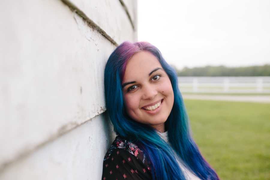 Twenty two year old who has over 20 suicide attempts in a year leans against wall smiling