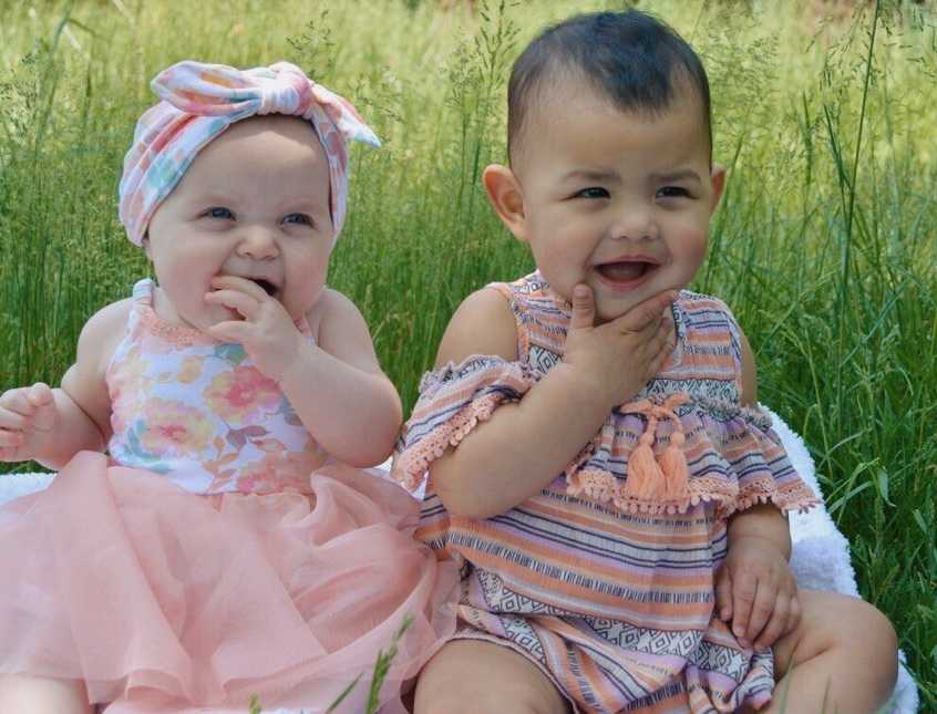 Infant sits in grass next to adopted infant sister parents adopted from couple at church