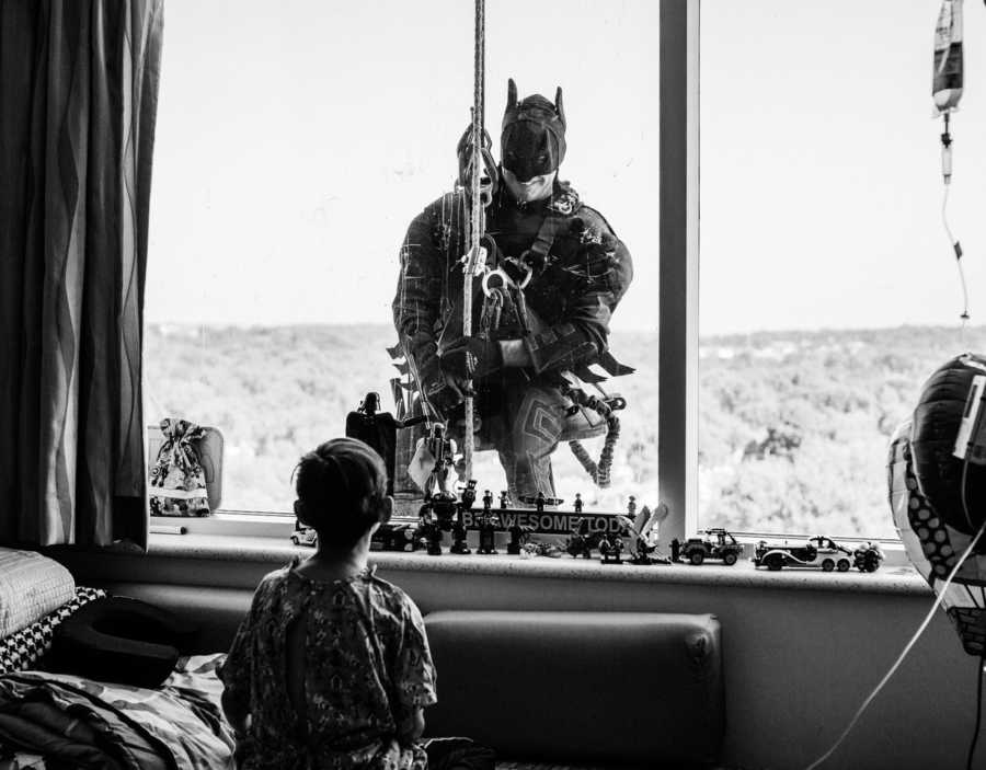 Young boy with heart issues sits in hospital looking out window to see window washer dressed as Batman