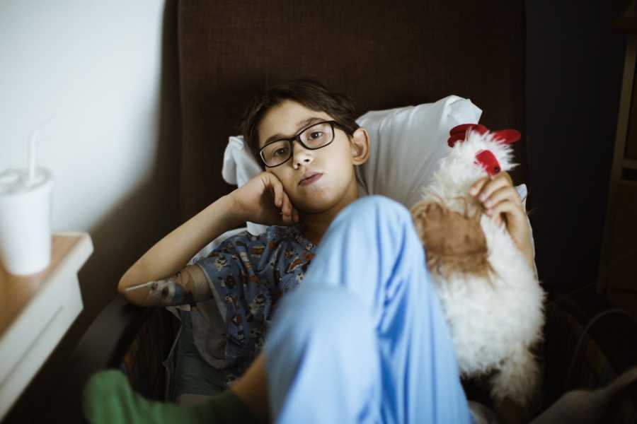 Young boy sits in hospital chair with stuffed animal recovering from heart surgery