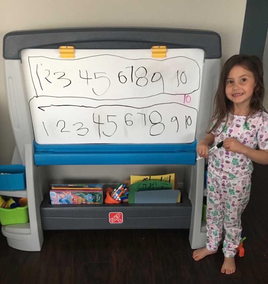 Little girl up for adoption who was described as "feral" stands next to white board smiling