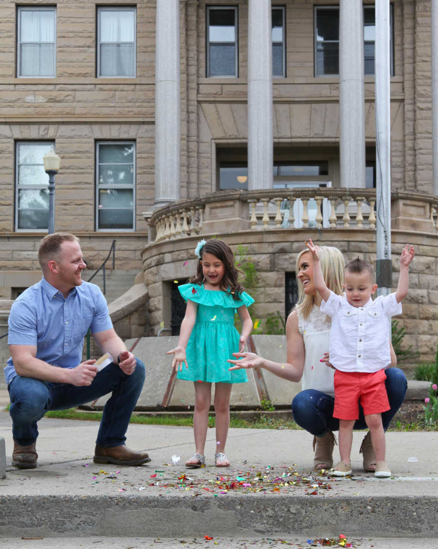 Mother and father stand with adopted daughter outside of adoption court with birth child throwing confetti