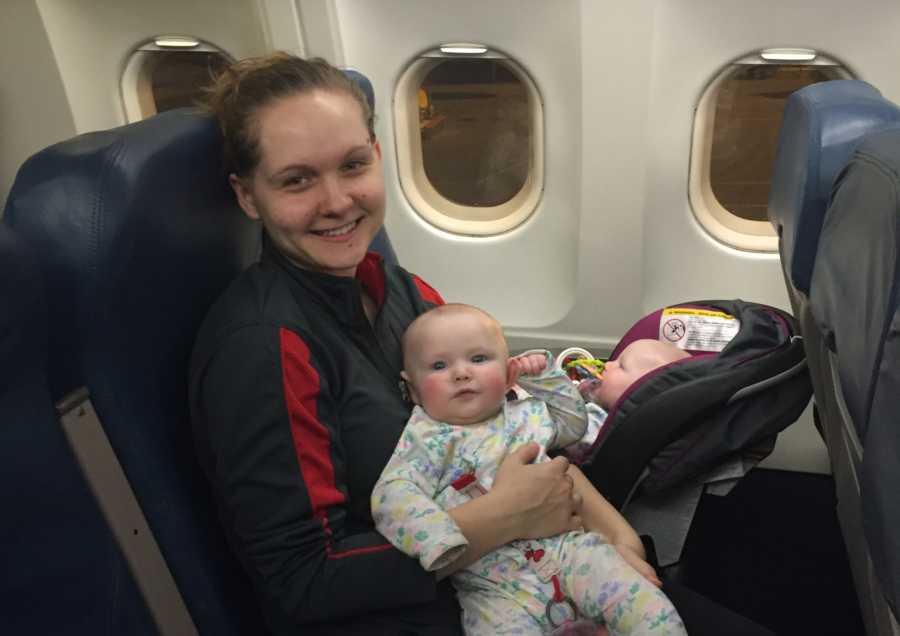 Mother traveling alone on plane with one infant twin in carseat on lap and other in her arms