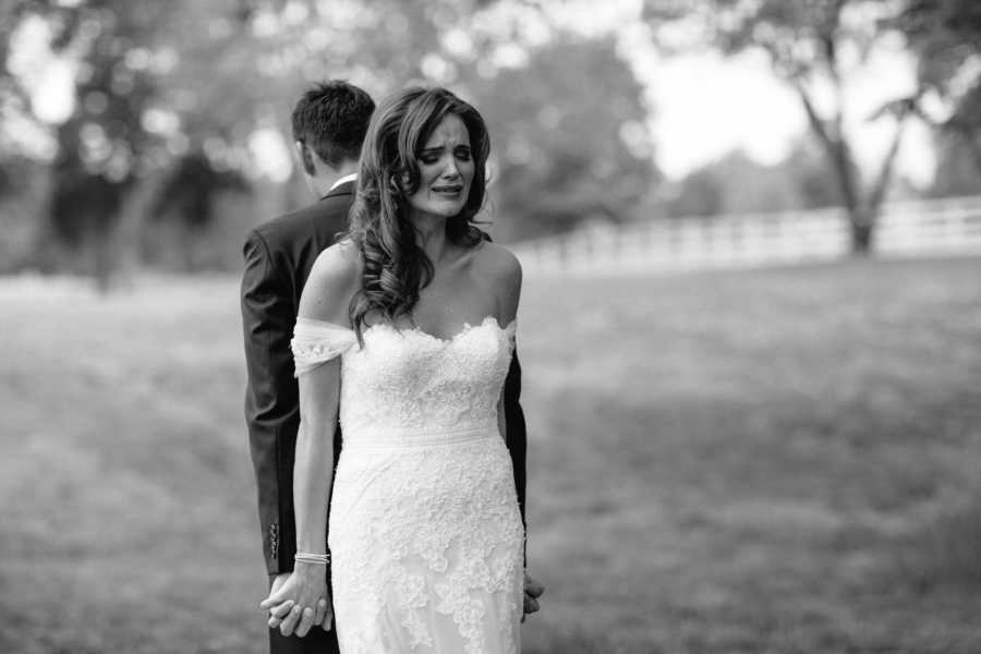 Bride cries while standing back to back with groom holding hands