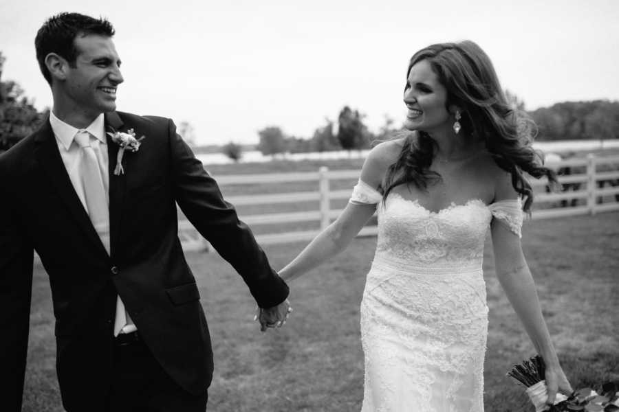 Bride and groom smile at each other as they walk hand in hand