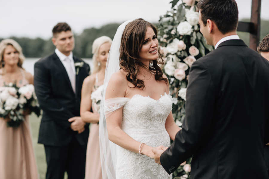 Bride cries while holding grooms hands at altar of outdoor wedding