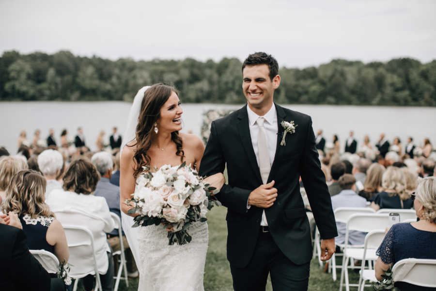 Bride and groom walk down aisle smiling after getting married outdoors near body of water
