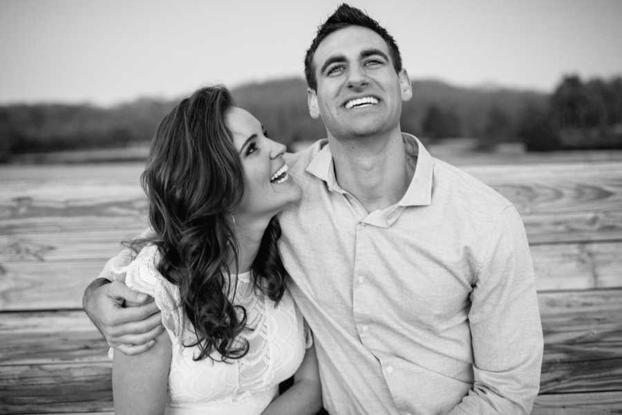 Man smiles with arm around girlfriend who is looking up smiling at him