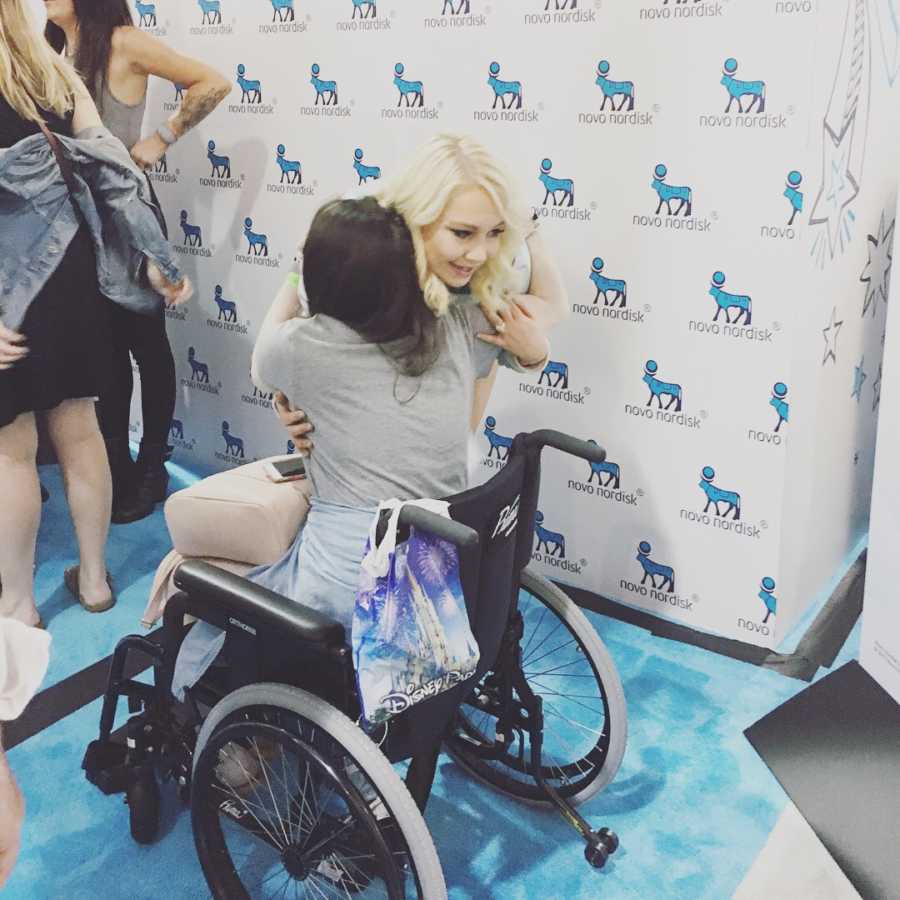 Woman leans over to hug woman in wheelchair with unknown illness