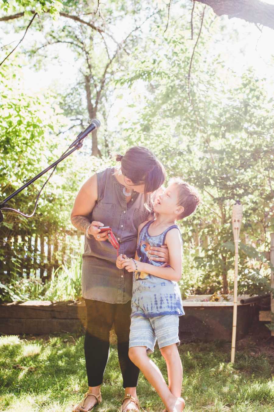 Foster mother stands outside with arm around son