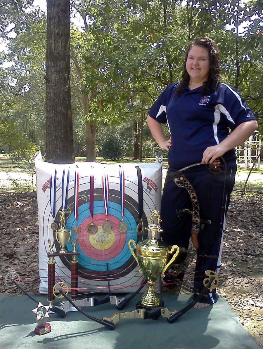 Teen stands with bow next to target with medals laying over it who has since passed from car crash