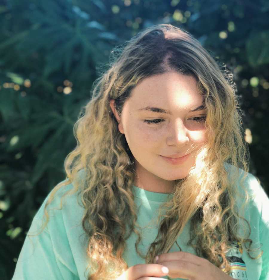 Young woman looks away from the camera and nervously plays with her blonde curly hair