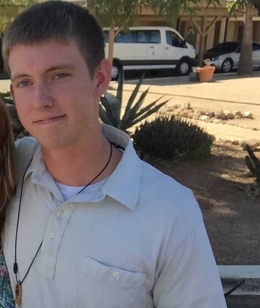 Young man smiles for a photo in light-colored button-down and long fish necklace