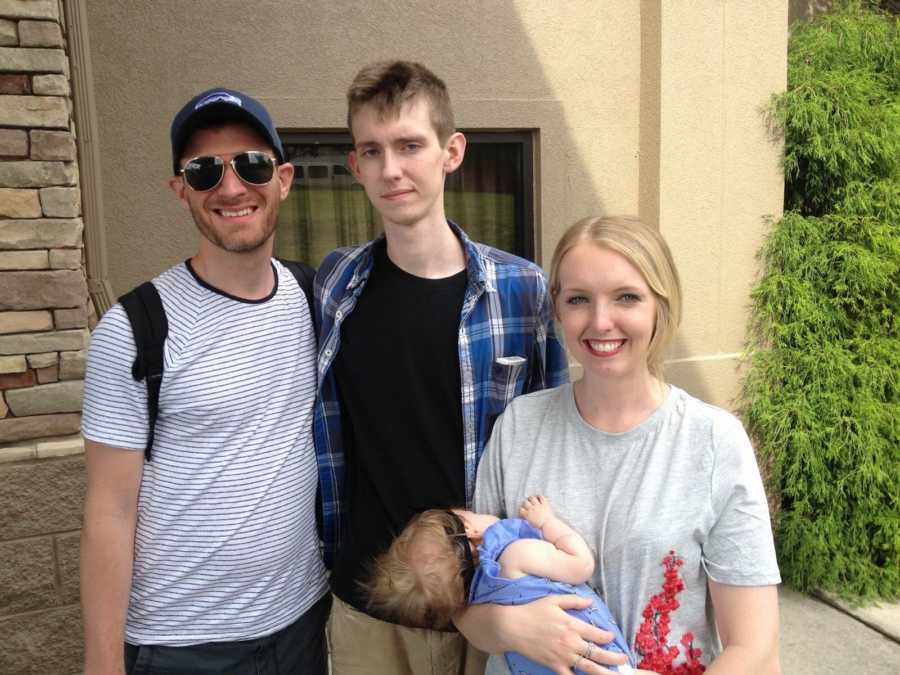 Woman holds newborn child while smiling for a photo with two men