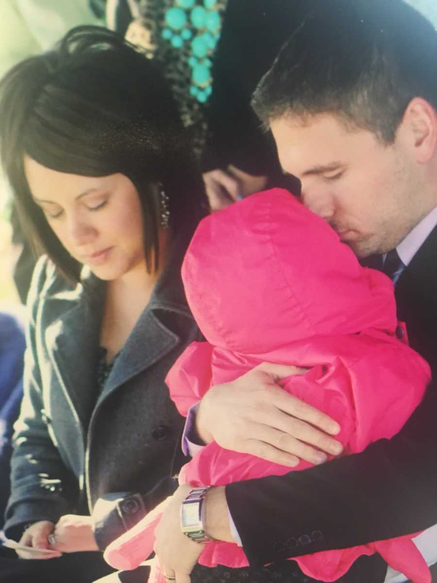 Wife and husband who holds their daughter close their eyes at their micro-preemie's burial