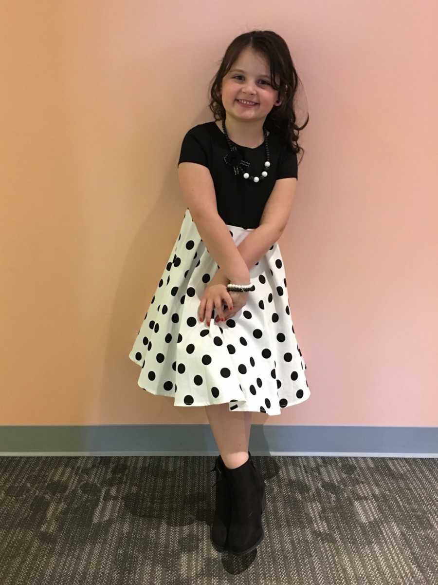 Little boy who became a girl smiling in black and white polka dot dress and boots