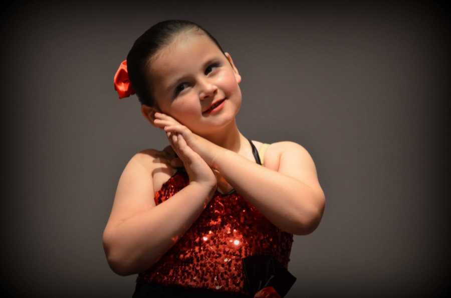 Little boy who is now a girl posing with hands rested on her cheek in dance recital costume