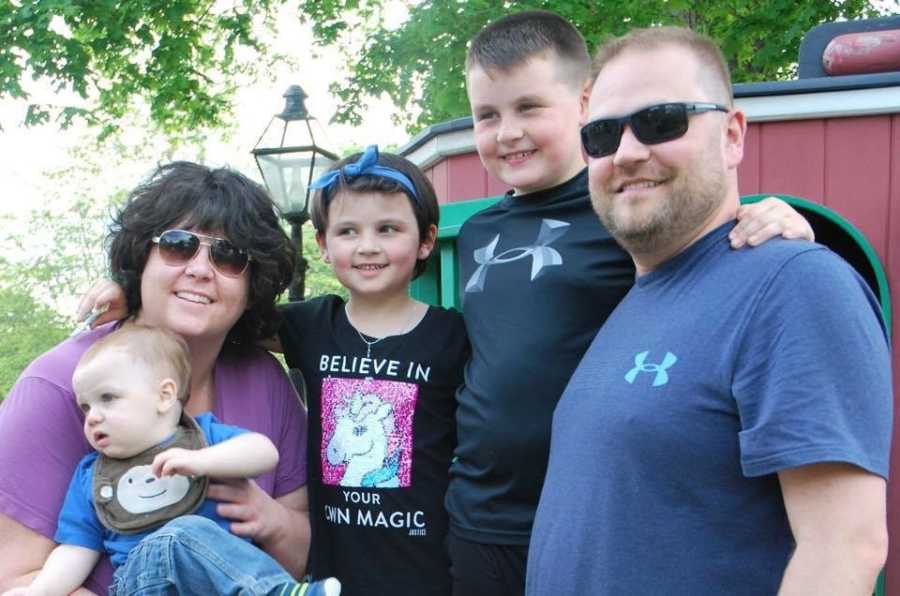 Little boy who is now a girl stands smiling with mother, father, and her two brothers