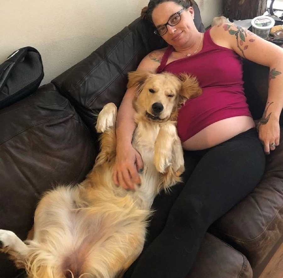 Pregnant woman who had hard time conceiving lies on couch with golden retreiver in lap 