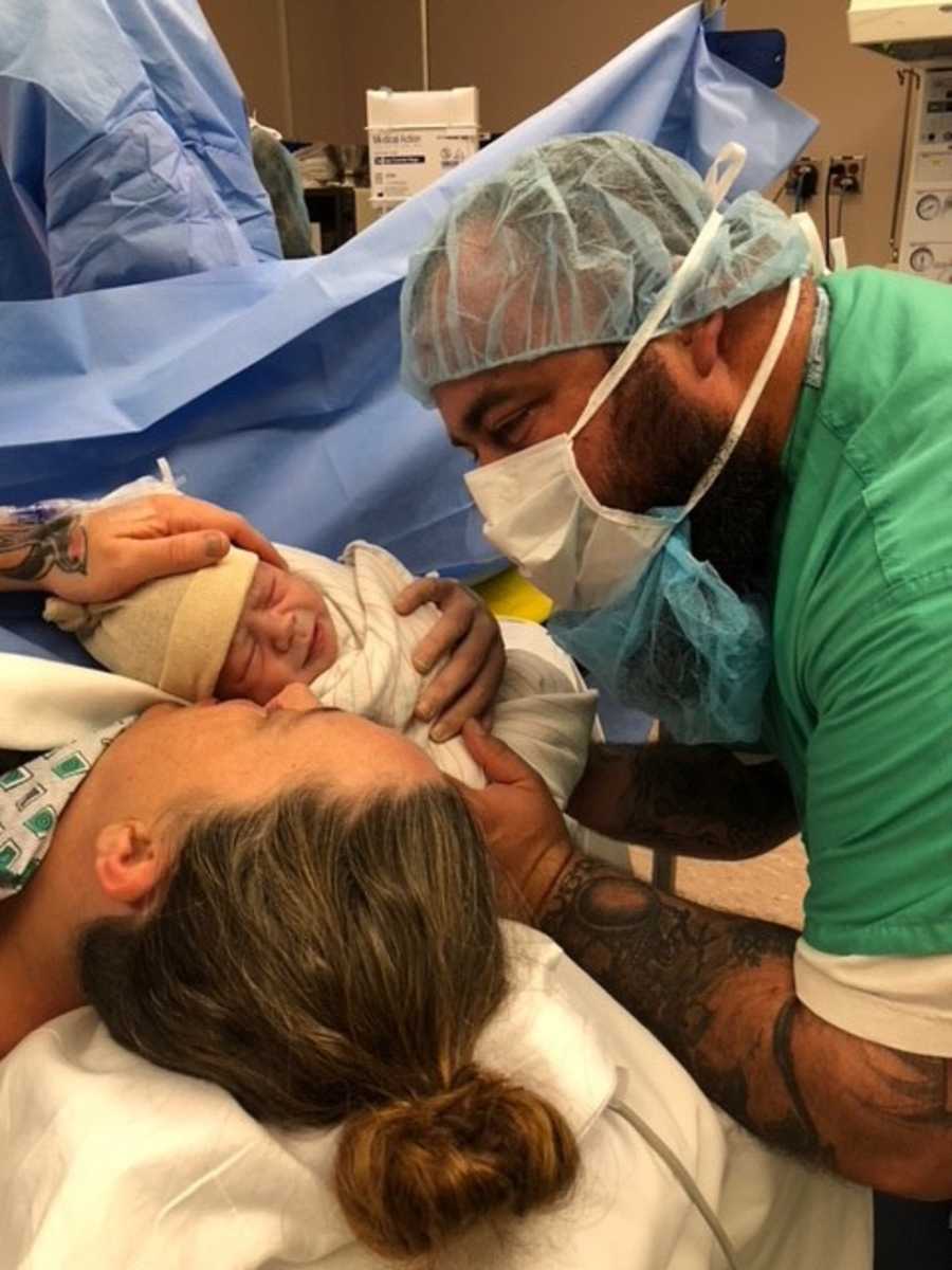 Husband leans over holding newborn beside wife who just had c-section
