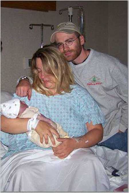 Husband and wife sit smiling in hospital bed holding newborn who will pass away few hours later