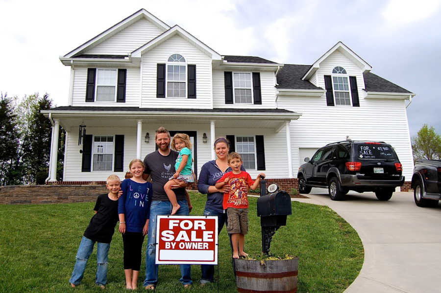 Husband and wife stand with their for kids by for sale sign in front of their home