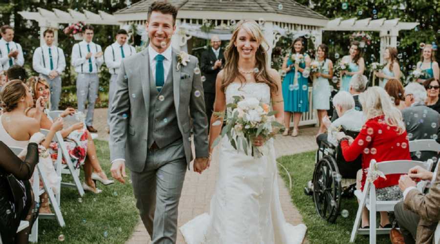 Bride with crohn's disease walks down aisle smiling with groom with wedding party in background
