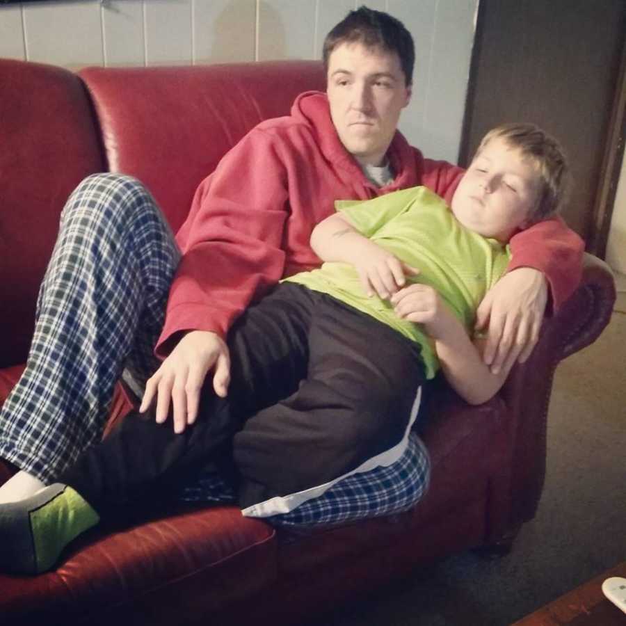 Father sits on couch with 7 year old son on his lap who mother wrote note to on his birthday