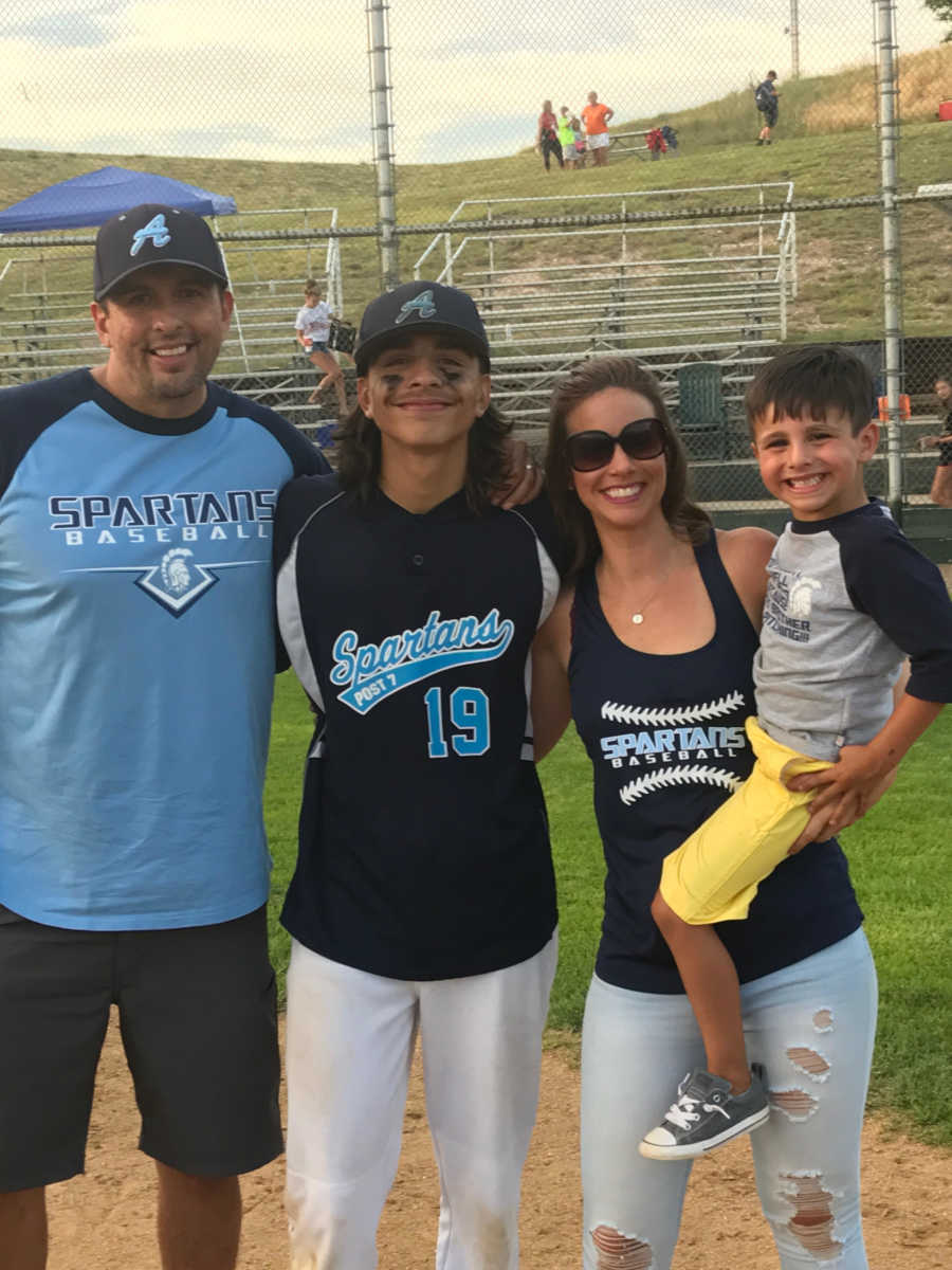 Mother holds son beside her stepson and husband at stepson's baseball game