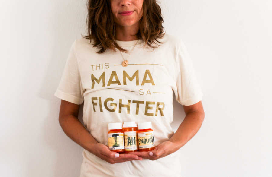 Woman with fertility struggles holds fertility medication bottles with words, "I am enough" on them