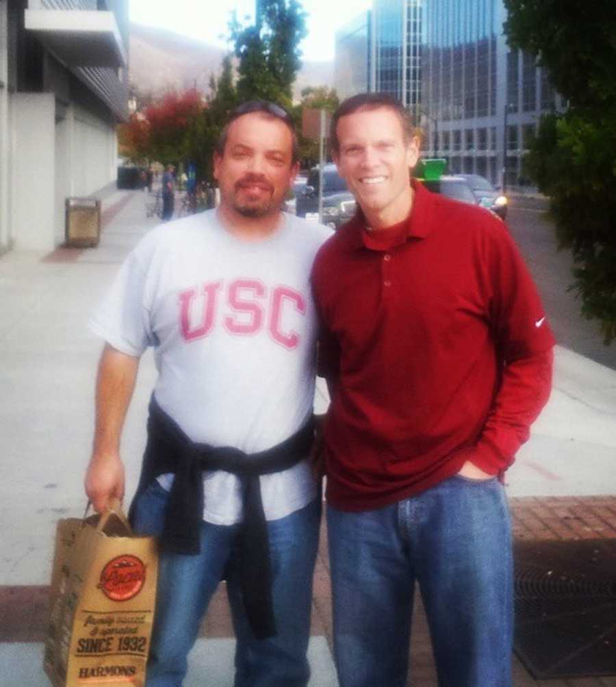 Childhood friends stand arm in arm smiling after running into each other on the street